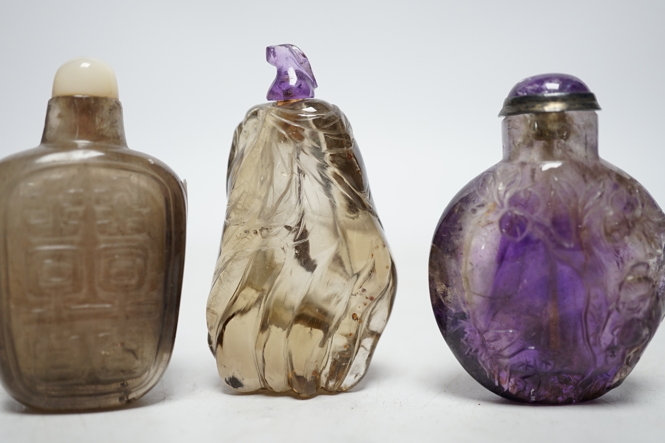 Three Chinese carved quartz snuff bottles, 19th/20th century to include a smoky quartz shuangxi bottle, an amethyst quartz bottle and a small smoky quartz gourd shaped bottle, largest 6.5cm high